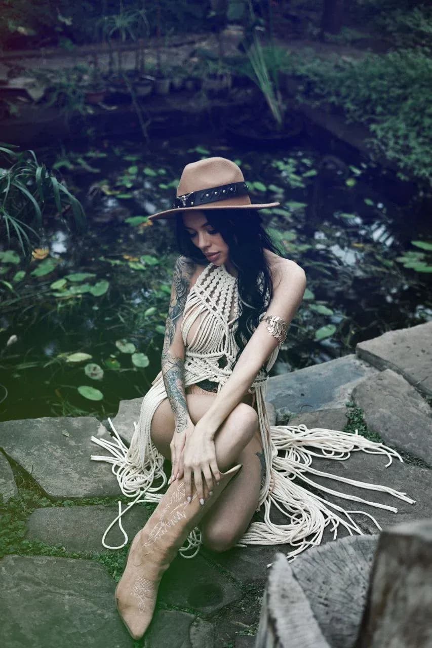 Модель в кружевном платье в бохо-стиле, сидящая на каменной стене рядом с ручьем