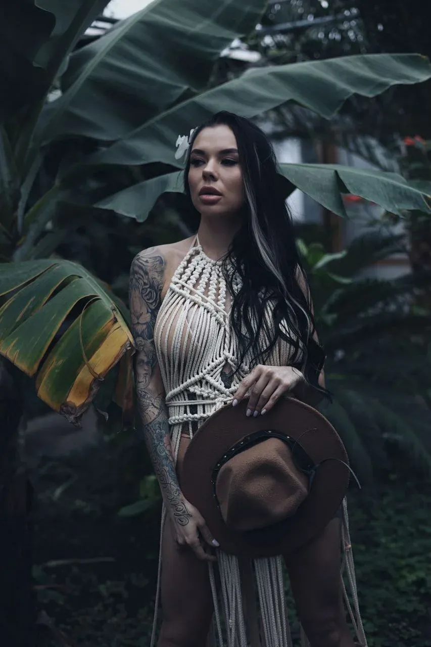 Женщина в бохо-топе и шляпе позирует на фоне тропической зелени